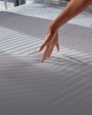Fingertips pressing into the QuickCool layer of the Nova Hybrid Snow mattress. 